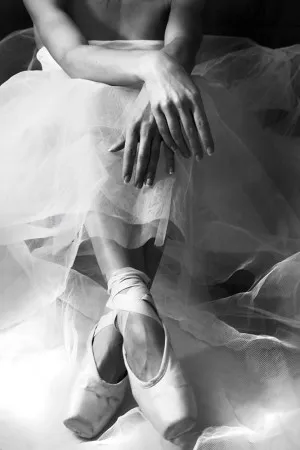 Verticale zwart-witfoto van een ballerina zittend buiten, met balletschoenen en elegante handen in detail