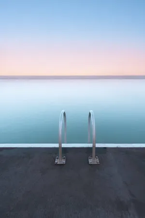 Verticale foto van een zwemmer bij een rotsbad in Newcastle, Australië tijdens schemering met zachte pastelkleuren