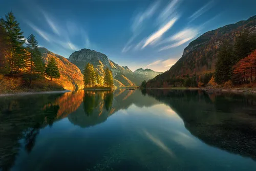 Horizontale foto van een stil meer met herfstbladeren en bergreflecties bij Lago del Predil in Italië