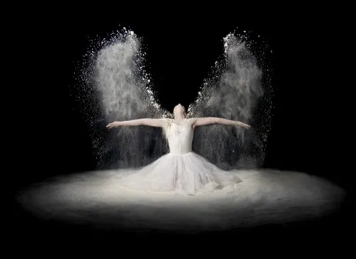 Horizontale fotografie van een vrouw met een jurk van bloemstof en veren, dansend in een buitenomgeving met spirituele en surrealistische elementen