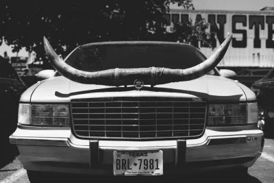 Zwart-wit foto van een geparkeerde vintage limousine met longhorn-hoorns in een buitenomgeving in Texas