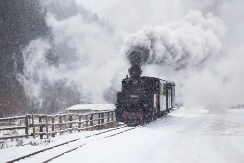 Horizontale foto van een oude stoomlocomotief bij een besneeuwd treinstation met rook en winterse sfeer