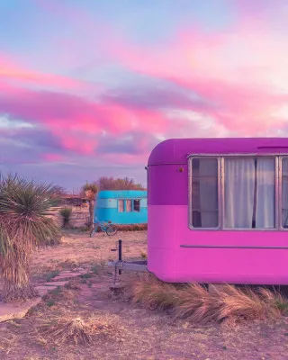 Verticale vintage camper in roze en blauw bij zonsondergang boven woestijnlandschap in Texas