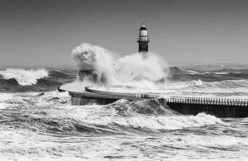 Zwart-wit fotografie van vuurtoren en woeste golven bij kustlijn Sunderland