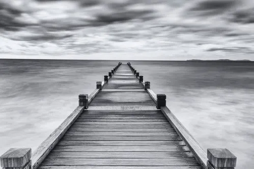 Zwart-wit fotografie van een houten steiger aan de kust van Saint Tropez met zee en wolken boven