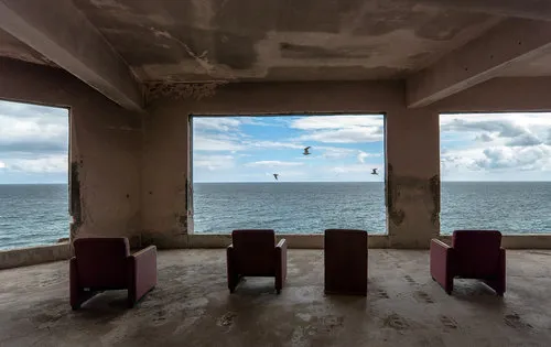 Fotografie van een vervallen bioscoop met oude stoel en ramen met uitzicht op zee en horizon