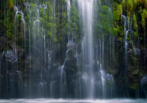 Horizontale foto van een kalme waterval die over mosbedekte rotsen stroomt in een groen landschap