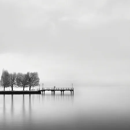 Zwart-wit foto van een stille pier aan Kastoria meer met bomen en zacht water