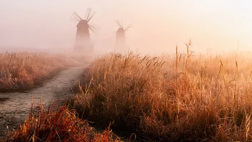 horizontale foto van een mistig landschap met windmolens en oude gebouwen in landelijke omgeving