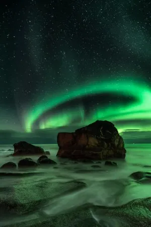 Verticaal landschapfoto van groene aurora borealis boven rotsachtige kust van Uttakleiv in Noorwegen