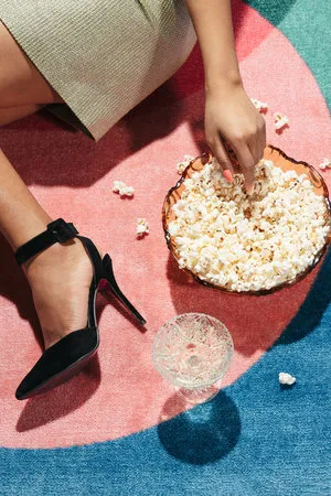 Verticale foto van een vrouw in pastelroze pumps met glas en popcorn in een retro outdoor setting