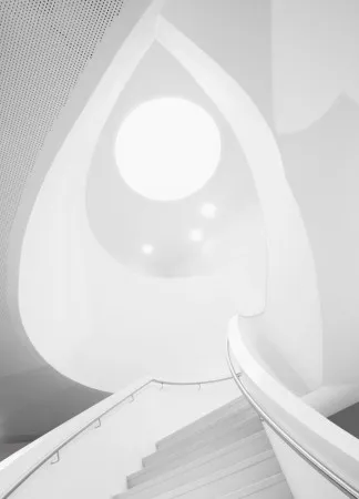 Zwart-wit verticale foto van een moderne trap met ronde vormen en helder wit interieur in Den Bosch