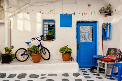 Horizontale foto van een kleurrijke Griekse binnenplaats met blauwe deuren, ramen, bloemen en een geparkeerde fiets