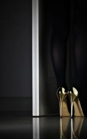 Verticale fotografie van gouden high heels en benen in een intieme interieur scène met deur en warme kleuren