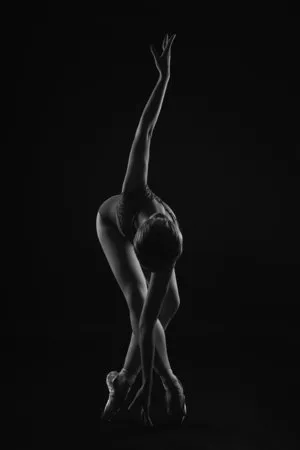 Verticale foto van een ballerina die op pointe shoes staat en haar arm om zich heen slaat