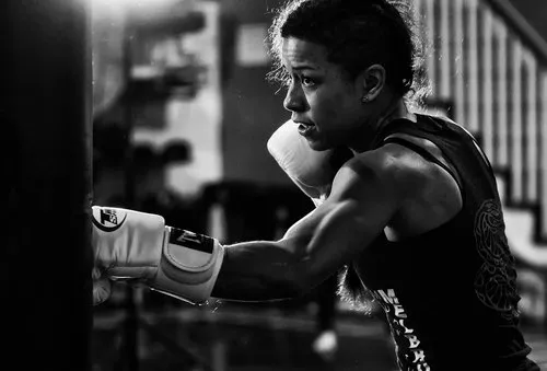 Zwart-witfoto van een vrouw die bokst tegen een bokszak tijdens intensieve training in een gym