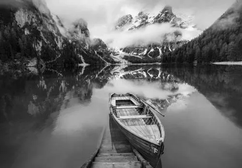 Zwart-wit horizontale foto van bergmeer Lago di Braies met roeiboot, houten trap en reflecties in het water