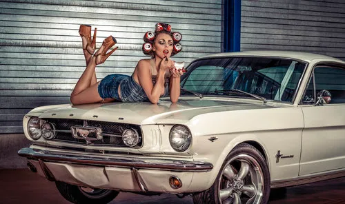Horizontale foto van retro pin-up vrouw liggend op motorkap klassieke Ford Mustang in parking garage