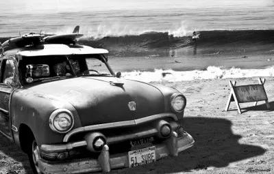 Zwart-wit foto van vintage Ford Woody auto bij Californische kust met surfers en golven