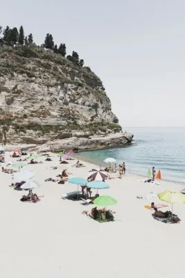 Verticale foto van een Italiaans strand met parasols, mensen, bergen en zee onder een lichte bewolkte lucht