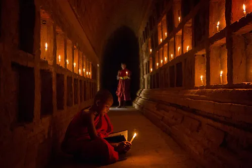 Horizontale foto van jonge monniken in een klooster, verdiept in studie bij zacht kaarslicht