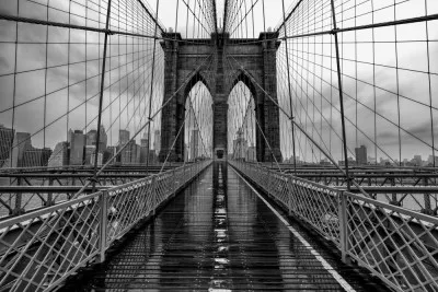 Zwart-wit foto van brooklyn bridge met symmetrische lijnen en new york skyline op achtergrond