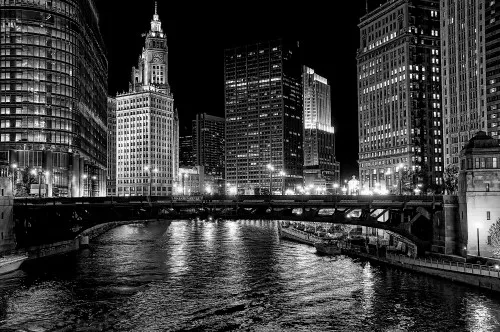 Zwart-wit fotografie van de Chicago River met skyline, brug en kloktoren tijdens de avond