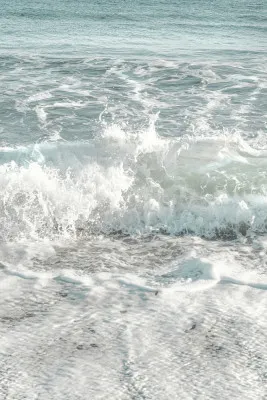 Verticale fotografie van een vervaagde kustlijn met golven die zacht over het zand rollen in zomers licht