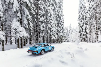 Horizontale foto van een blauwe Porsche 911 rallye in een besneeuwd boslandschap tijdens een race