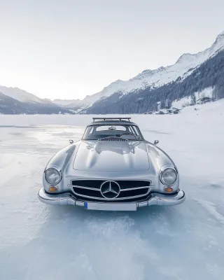 Verticale foto van een retro zilveren auto op een bevroren bergmeer met besneeuwde Alpen op de achtergrond