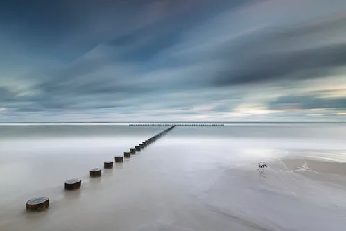 Horizontale foto van rustige kustlijn met blauwe zee en waterbrekers bij zonsopgang in Jaroslawiec, Polen