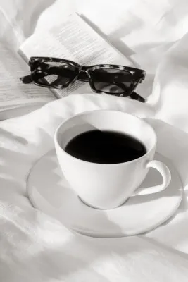 Monochrome verticale foto van koffie en boek op wit beddengoed in zachte ochtendlicht sfeer