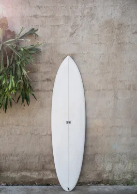 Verticale fotografie van een witte surfplank tegen een gevel met planten en moderne architectuur in neutrale kleuren
