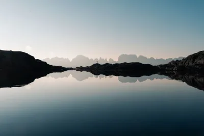 Horizontale foto van een persoon bij een bergmeer in de Dolomieten met spiegeling en bergen op de achtergrond
