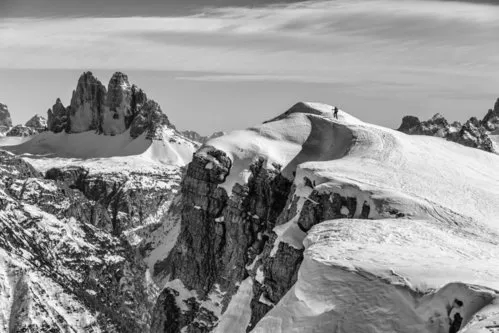 Zwart-wit foto van een wandelaar op een bergtop met sneeuw en bergen op de achtergrond